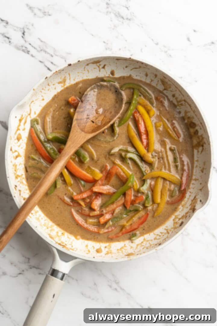 Overhead view of coconut milk being poured into the skillet with sautéed peppers and seasoning for the creamy Rasta Pasta sauce.