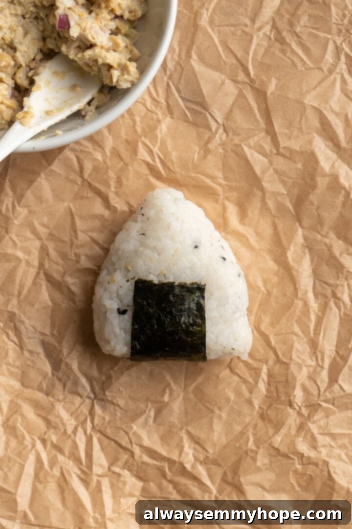 A finished vegan onigiri with its nori wrapper, resting on parchment paper, showcasing the simple elegance of this Japanese rice ball.