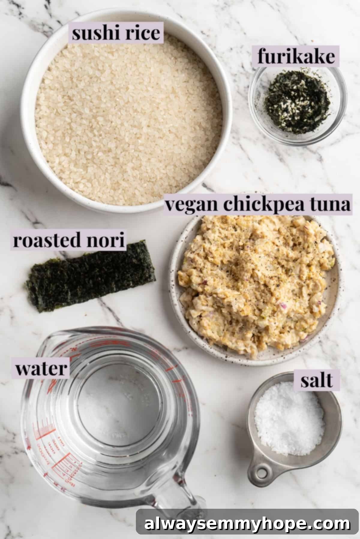 An overhead shot showcasing all the fresh, labeled ingredients required for making homemade vegan onigiri, including sushi rice, nori, furikake, and chickpea tuna.