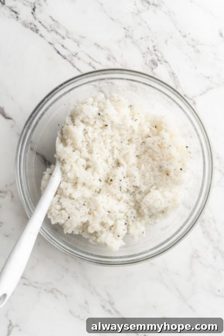 A large bowl filled with fluffy, seasoned sushi rice, ready for shaping, with a serving spoon resting beside it.