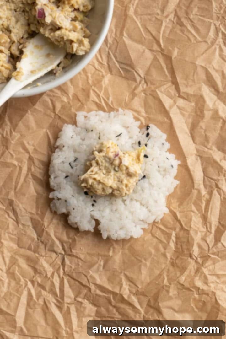 A scoop of vegan chickpea tuna filling placed neatly on a bed of seasoned sushi rice, ready for shaping into an onigiri.
