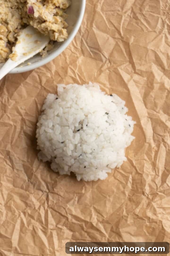 An onigiri in the process of being shaped, showing the chickpea tuna filling fully enclosed within the sushi rice, forming a compact rice ball.