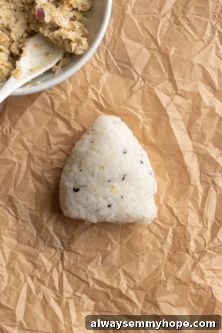A perfectly formed homemade vegan onigiri, shaped into a triangle, sitting on a piece of parchment paper before the nori wrapper is added.
