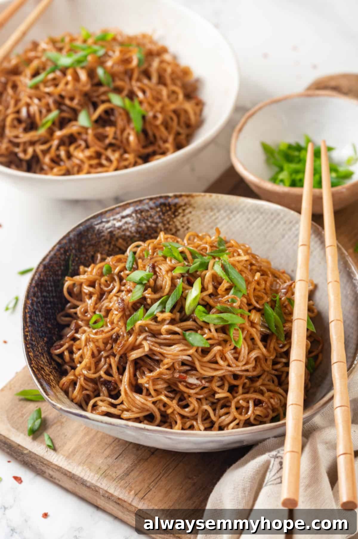 This spicy ramen recipe is an easy budget-friendly dinner that's packed with flavour! Sweet, spicy and umami—and it takes minutes to make! Two bowls of spicy ramen with small bowl of green onions