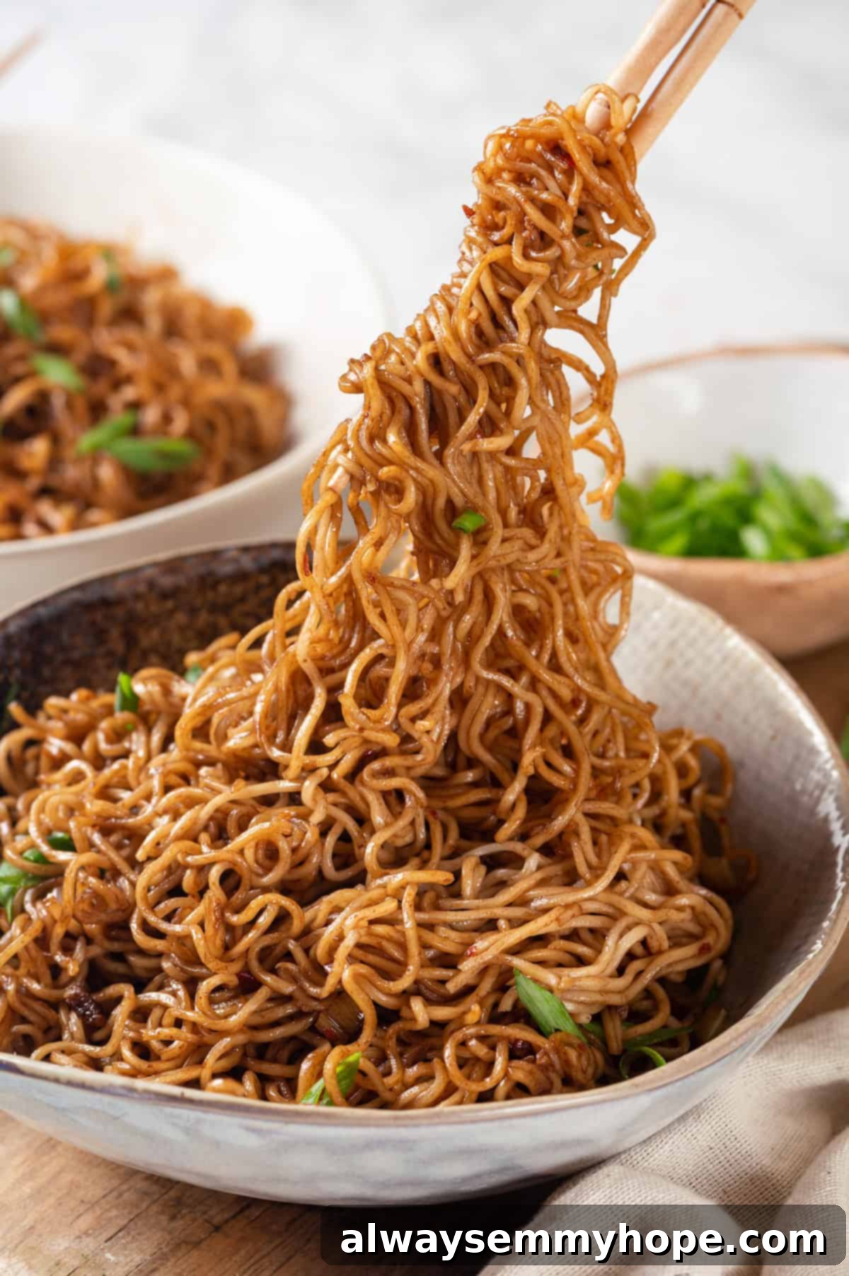 This spicy ramen recipe is an easy budget-friendly dinner that's packed with flavour! Sweet, spicy and umami—and it takes minutes to make! Spicy ramen being lifted from bowl with chopsticks