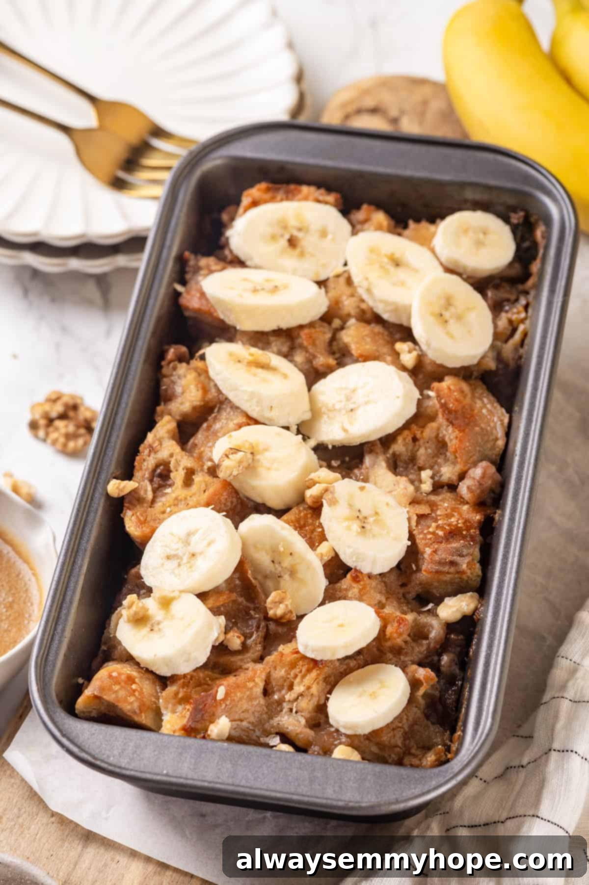An overhead shot of the baked vegan banana bread pudding in a loaf pan, beautifully golden, with fresh banana slices arranged on top.