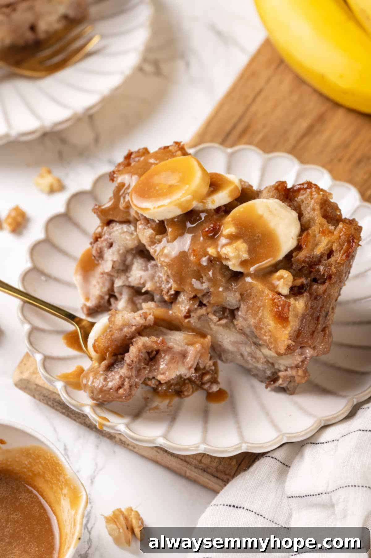 A fork sinking into a warm, tender piece of vegan banana bread pudding on a white plate, highlighting its rich, custardy texture.