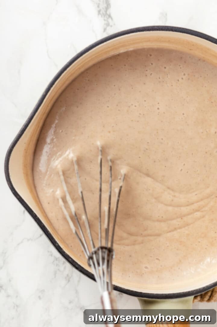 Overhead view of the custard in a saucepan, being whisked to thicken over low heat for banana bread pudding.