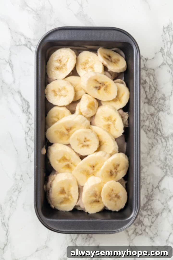 Overhead view of the first layer of sliced bananas spread evenly in a loaf pan for banana bread pudding.