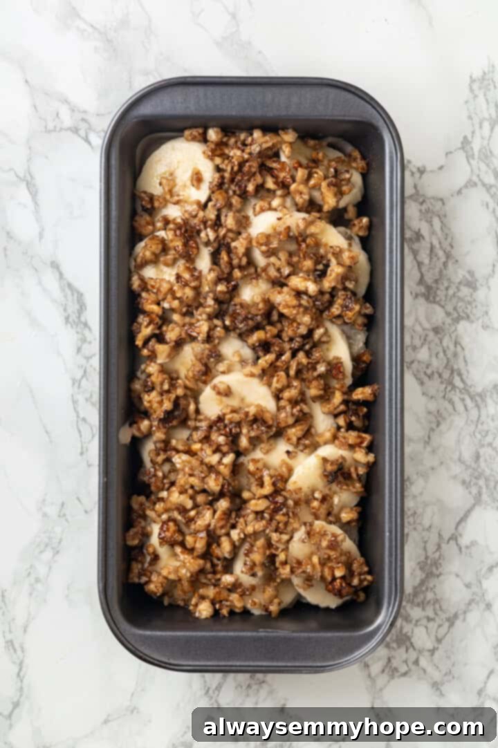 Overhead view of the walnut and bread layers being added on top of the bananas in the loaf pan for banana bread pudding.