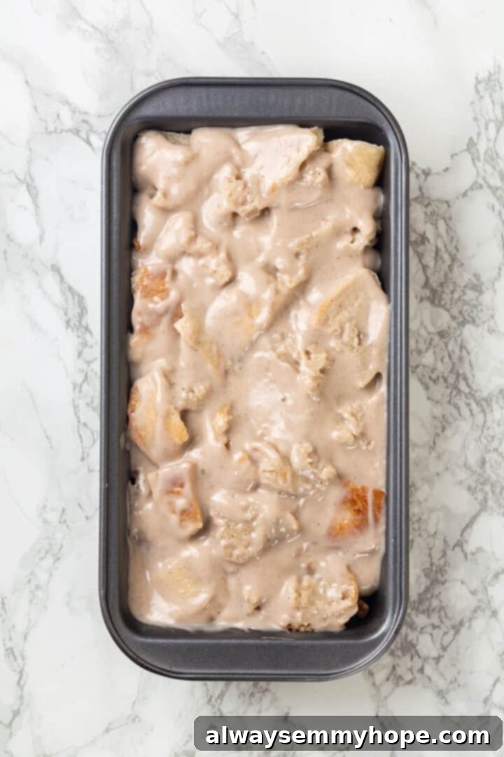 Overhead view of the fully assembled and unbaked banana bread pudding in a loaf pan, showcasing the custard-soaked bread and visible fruit.