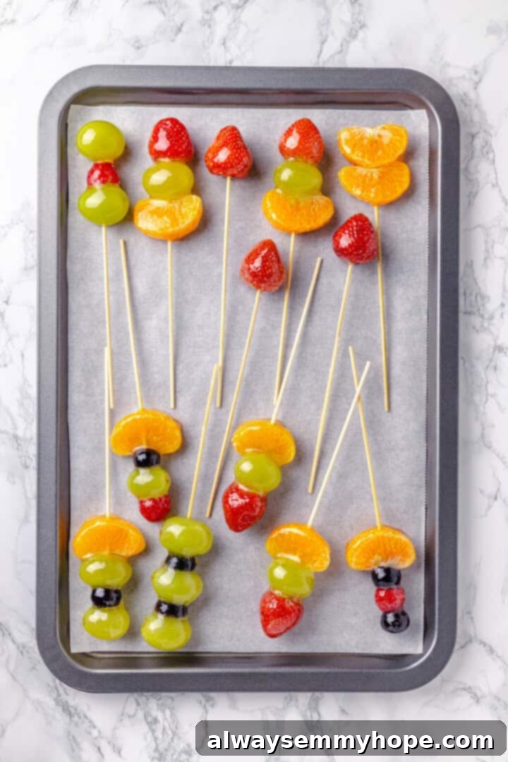 Tanghulu is one part fruit, one part candy and entirely delicious! Fruit skewers dipped in candy coating to create a sweet, crunchy shell. Overhead view of tanghulu drying on parchment-lined baking sheet
