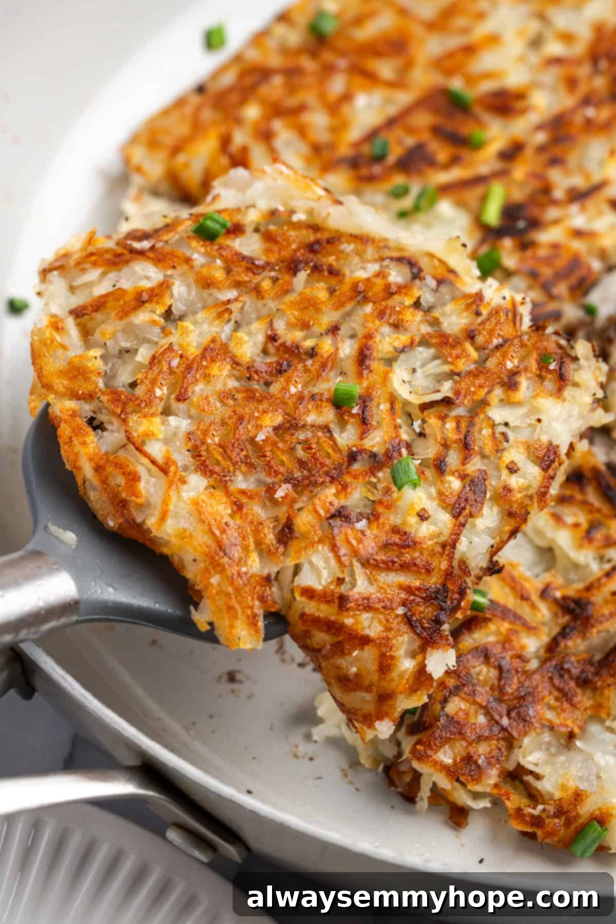 A spatula lifting a perfectly crispy hash brown from a hot skillet, showing its golden-brown underside.