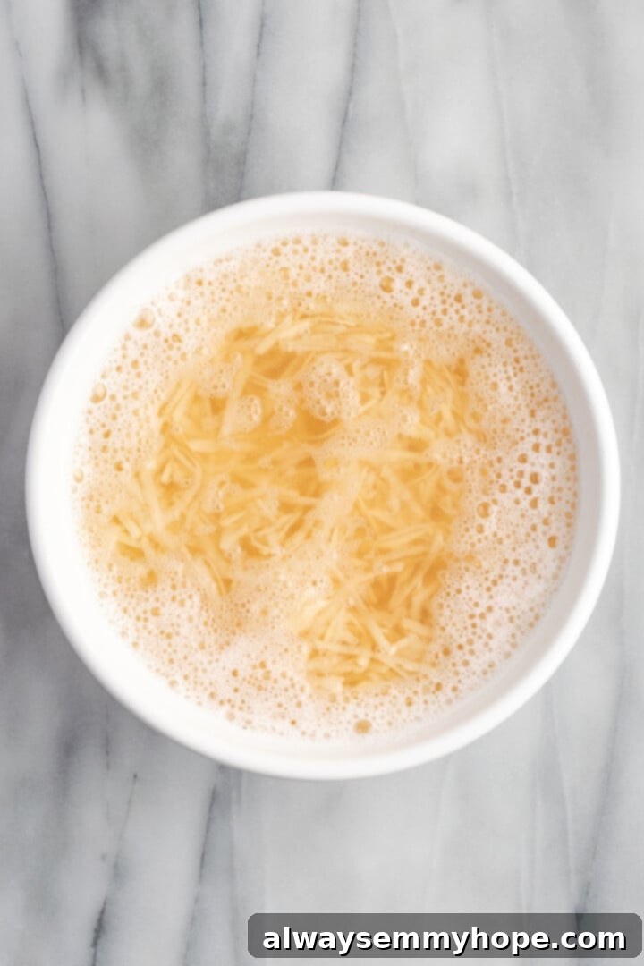 Shredded potatoes soaking in a bowl of cool water to remove excess starch.