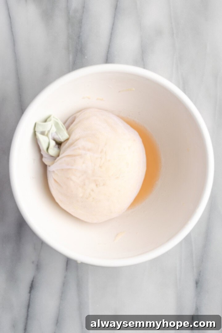 Shredded potatoes wrapped in a cheesecloth, held over a bowl, illustrating the process of squeezing out excess liquid.