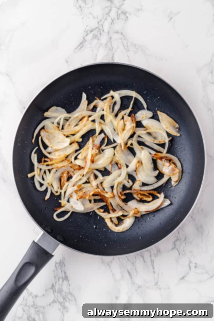 This vegan birria pizza recipe has all the savory, spicy goodness and toppings of birria tacos, but in the form of a cheesy pizza! Overhead view of onions caramelizing in a black skillet on the stovetop