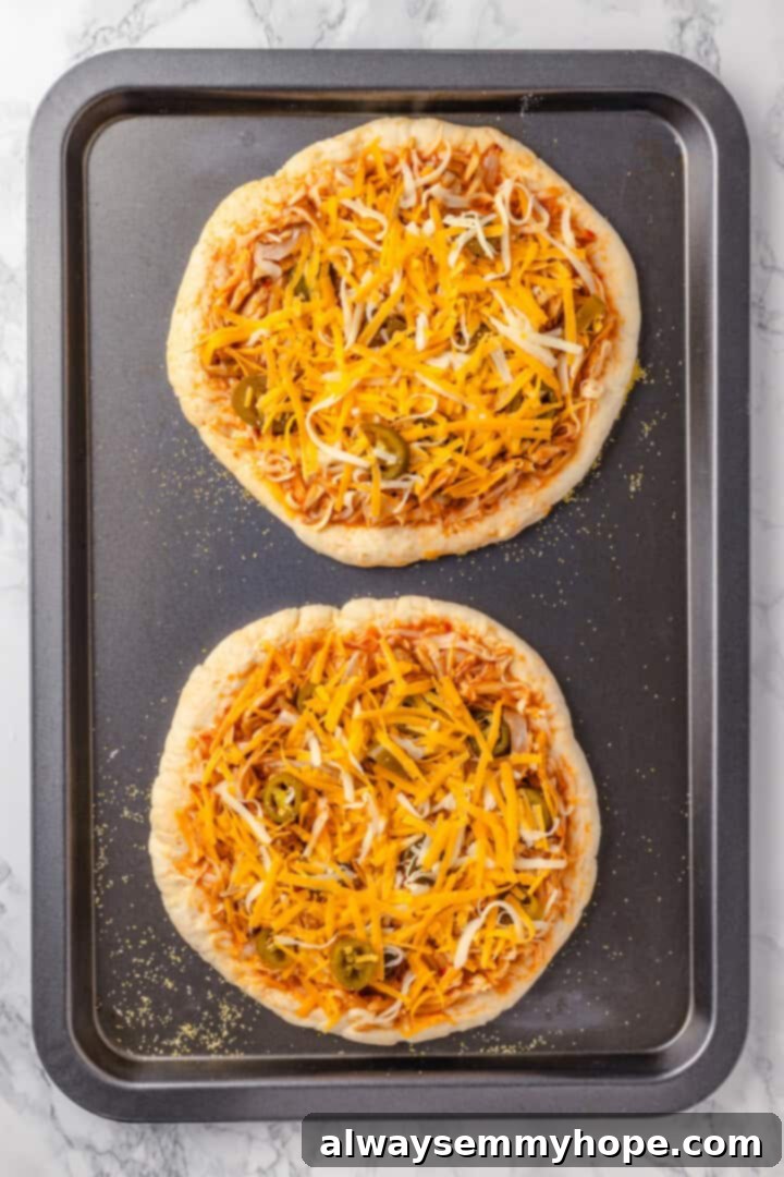 This vegan birria pizza recipe has all the savory, spicy goodness and toppings of birria tacos, but in the form of a cheesy pizza! Two unbaked vegan birria pizzas on a sheet pan, ready for the oven