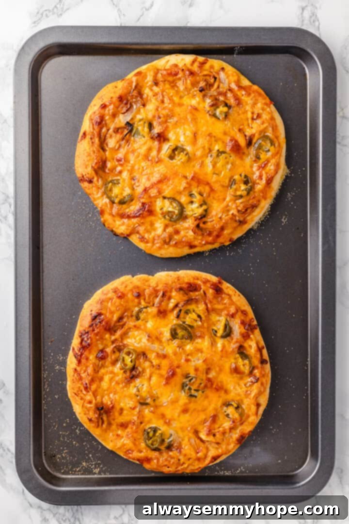 This vegan birria pizza recipe has all the savory, spicy goodness and toppings of birria tacos, but in the form of a cheesy pizza! Two freshly baked vegan birria pizzas on a sheet pan, with melted cheese and crispy crusts