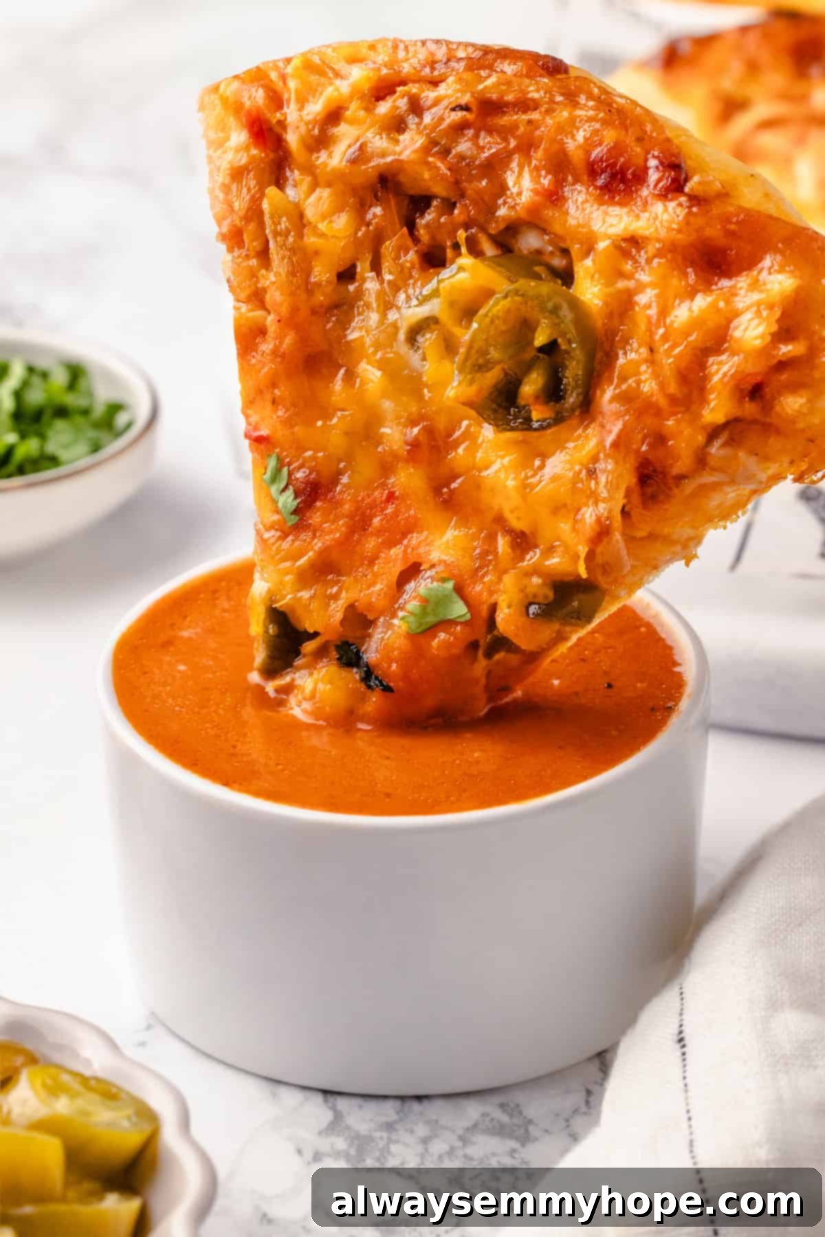 This vegan birria pizza recipe has all the savory, spicy goodness and toppings of birria tacos, but in the form of a cheesy pizza! Close-up of a hand dipping a slice of vegan birria pizza into a small bowl of birria broth