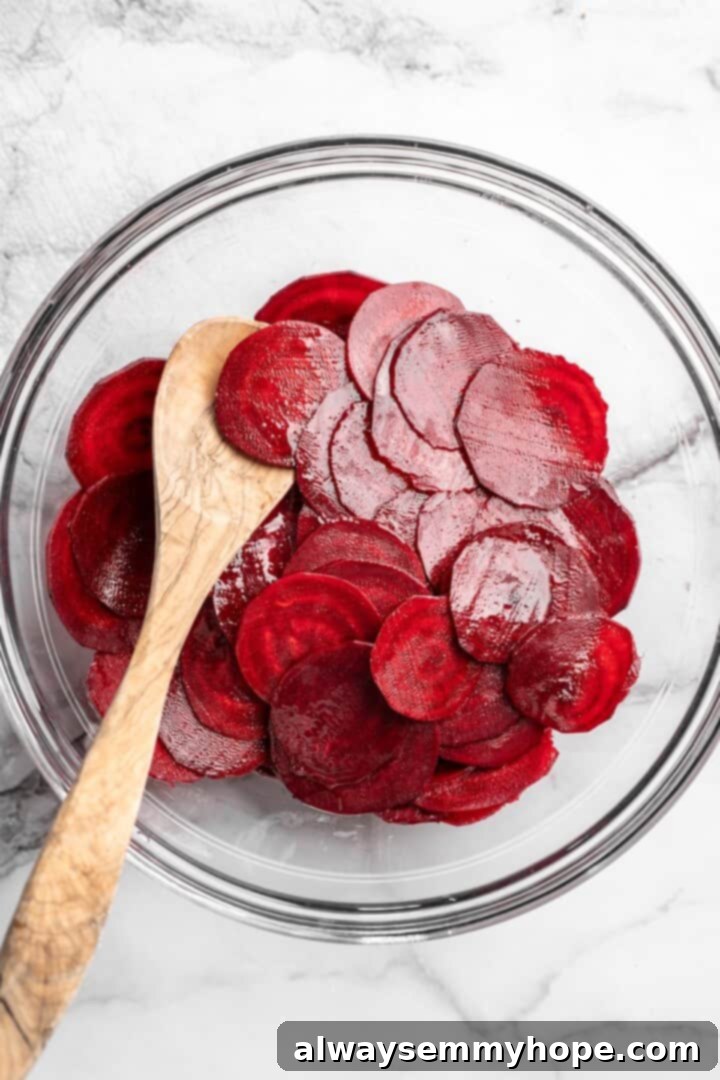 Overhead view of raw beet slices in bowl with wooden spoon