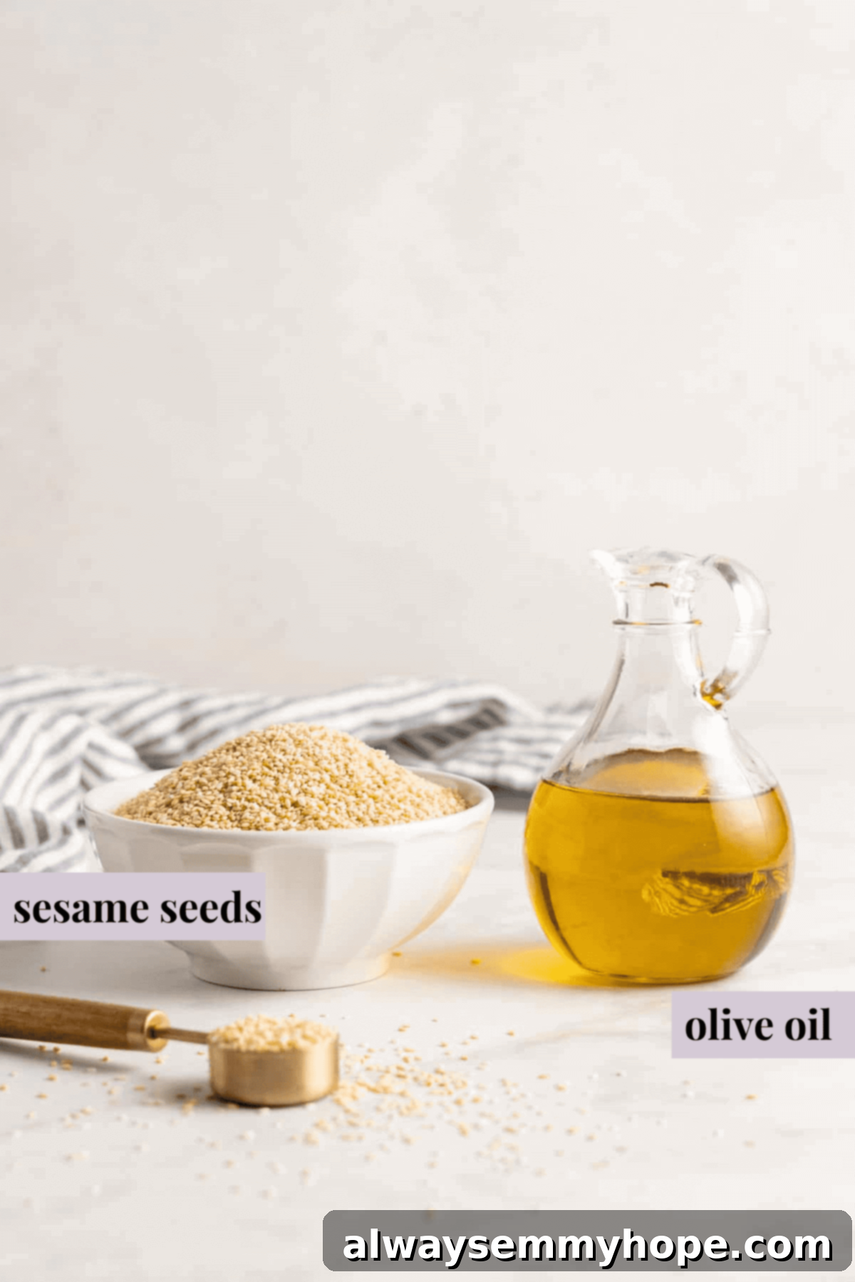 You’re two ingredients away from homemade tahini! Make it yourself and you’ll save so much money. Use in hummus, salad dressings, and more! An overhead shot shows a rustic wooden bowl filled with plain sesame seeds, positioned next to a clear glass pitcher holding golden olive oil. These are the two essential ingredients for making homemade tahini.