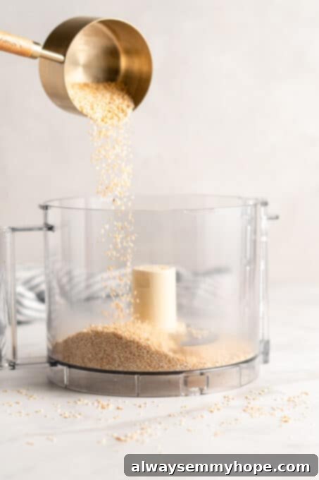 You’re two ingredients away from homemade tahini! Make it yourself and you’ll save so much money. Use in hummus, salad dressings, and more! A measuring cup of toasted sesame seeds is being poured into the bowl of a food processor, signaling the start of the blending process for homemade tahini.