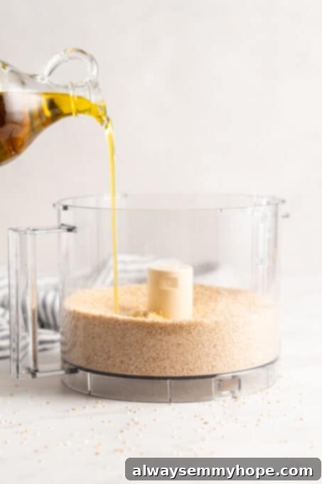 You’re two ingredients away from homemade tahini! Make it yourself and you’ll save so much money. Use in hummus, salad dressings, and more! Olive oil is being carefully poured from a glass pitcher into a food processor bowl already containing toasted sesame seeds, illustrating the next step in creating smooth tahini.