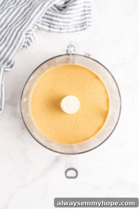 You’re two ingredients away from homemade tahini! Make it yourself and you’ll save so much money. Use in hummus, salad dressings, and more! An overhead view captures the creamy, smooth texture of freshly made tahini swirling in the bowl of a food processor, indicating it has reached the perfect consistency.