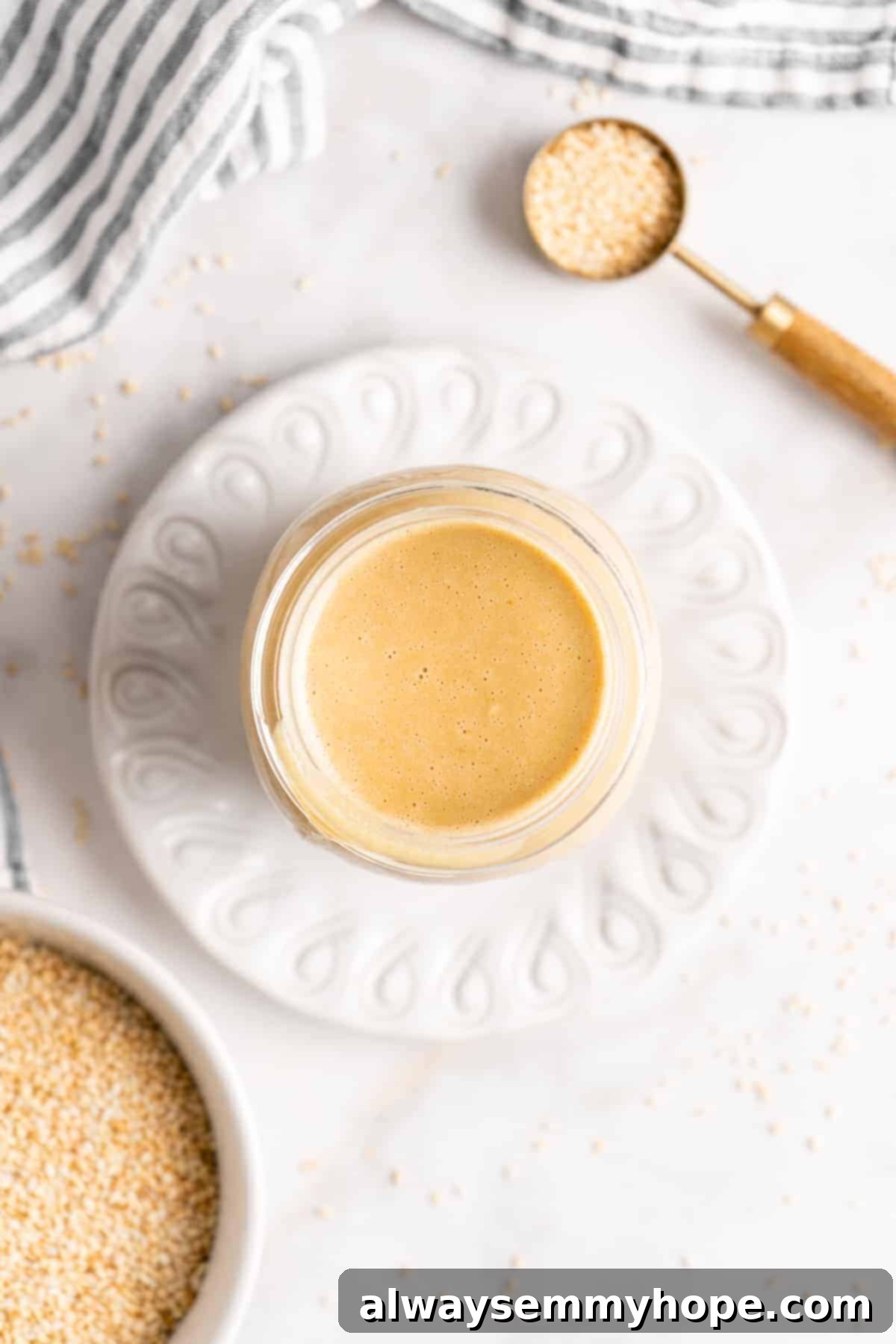 You’re two ingredients away from homemade tahini! Make it yourself and you’ll save so much money. Use in hummus, salad dressings, and more! An overhead shot displays a clear glass jar filled with smooth, golden homemade tahini, highlighting its fresh and inviting texture, ready for use or storage.