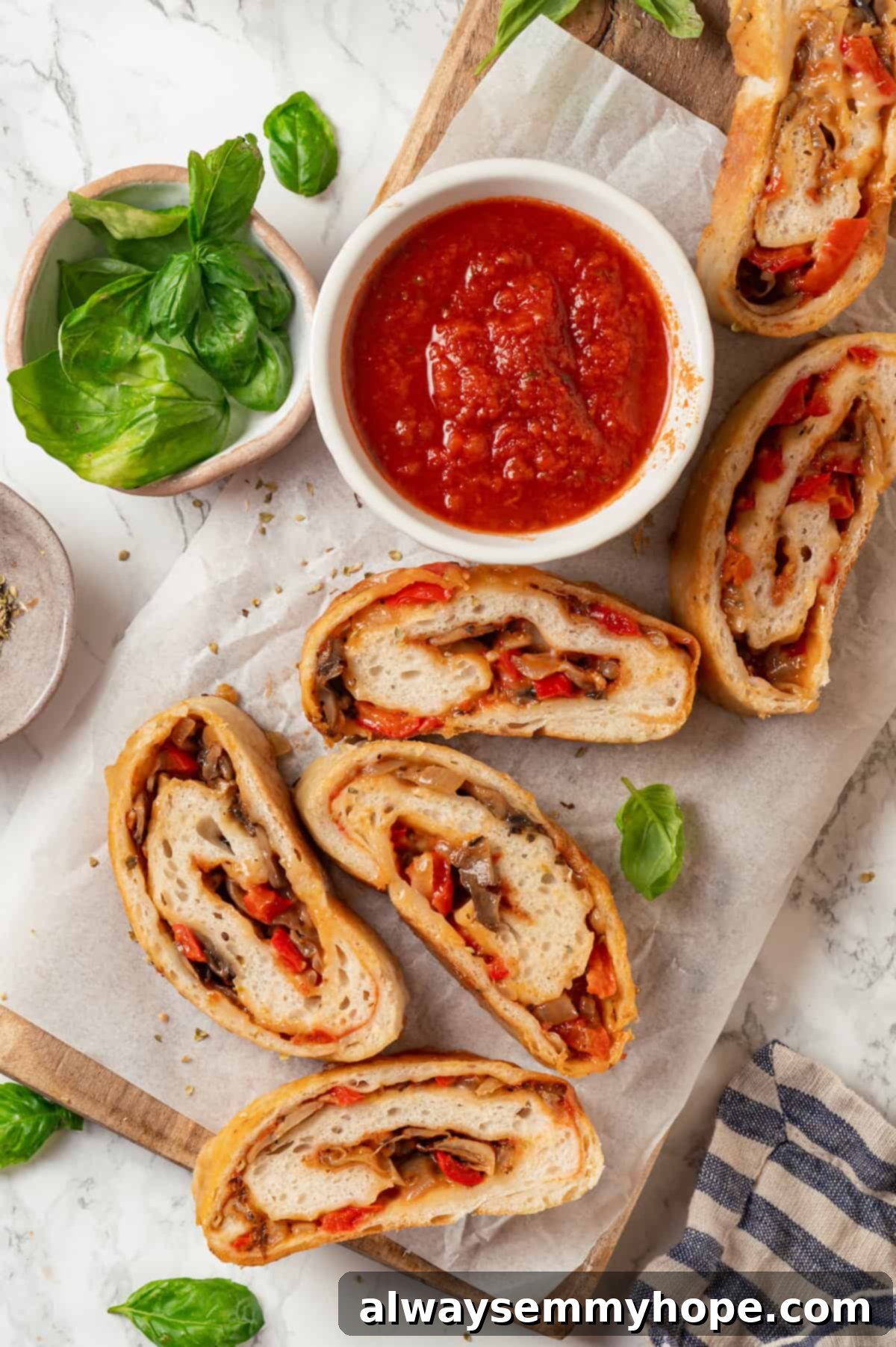 This vegan stromboli recipe is like a giant pizza roll, with marinara, plant-based cheese and veggies baked inside a golden brown crust. Yum! Overhead view of sliced stromboli on wooden board with bowl of marinara