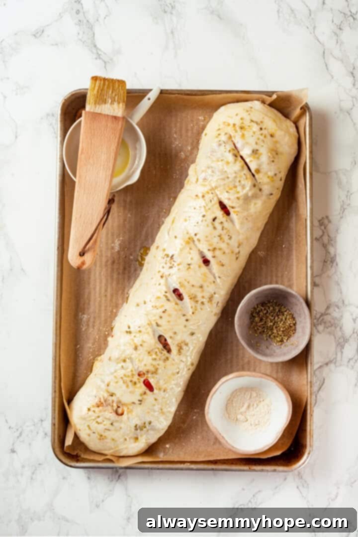 This vegan stromboli recipe is like a giant pizza roll, with marinara, plant-based cheese and veggies baked inside a golden brown crust. Yum! Overhead view of stromboli on sheet pan before baking