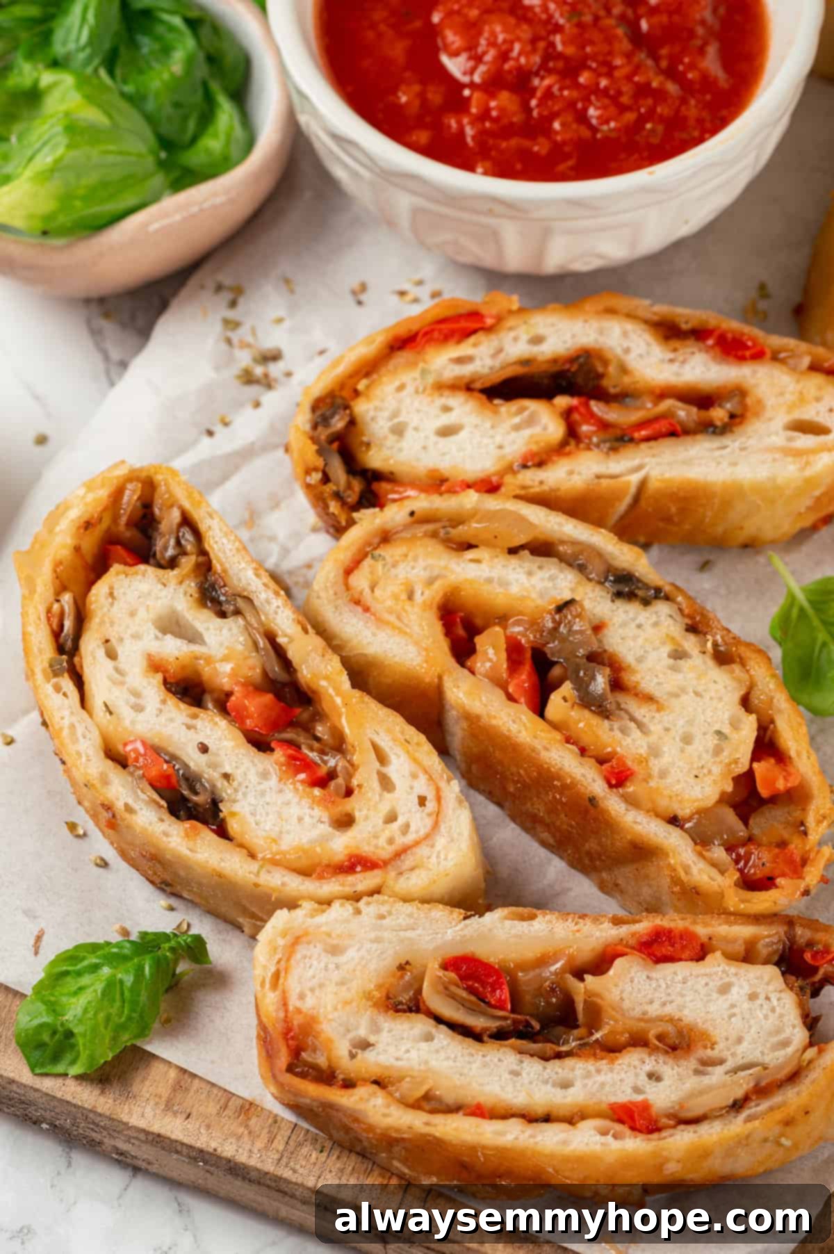 This vegan stromboli recipe is like a giant pizza roll, with marinara, plant-based cheese and veggies baked inside a golden brown crust. Yum! Top-down view of vegan stromboli slices on wood board with marinara in bowl