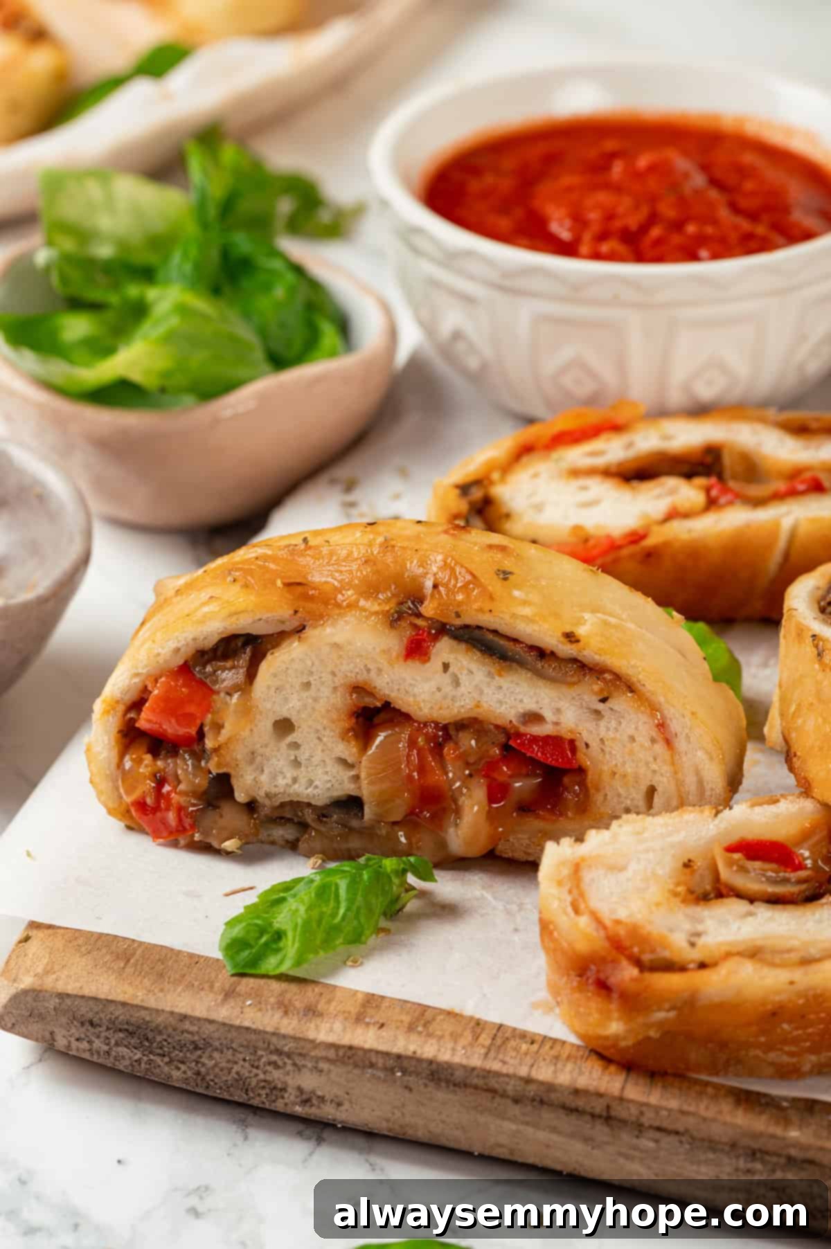 This vegan stromboli recipe is like a giant pizza roll, with marinara, plant-based cheese and veggies baked inside a golden brown crust. Yum! Stromboli slices on wooden board with bowl of sauce