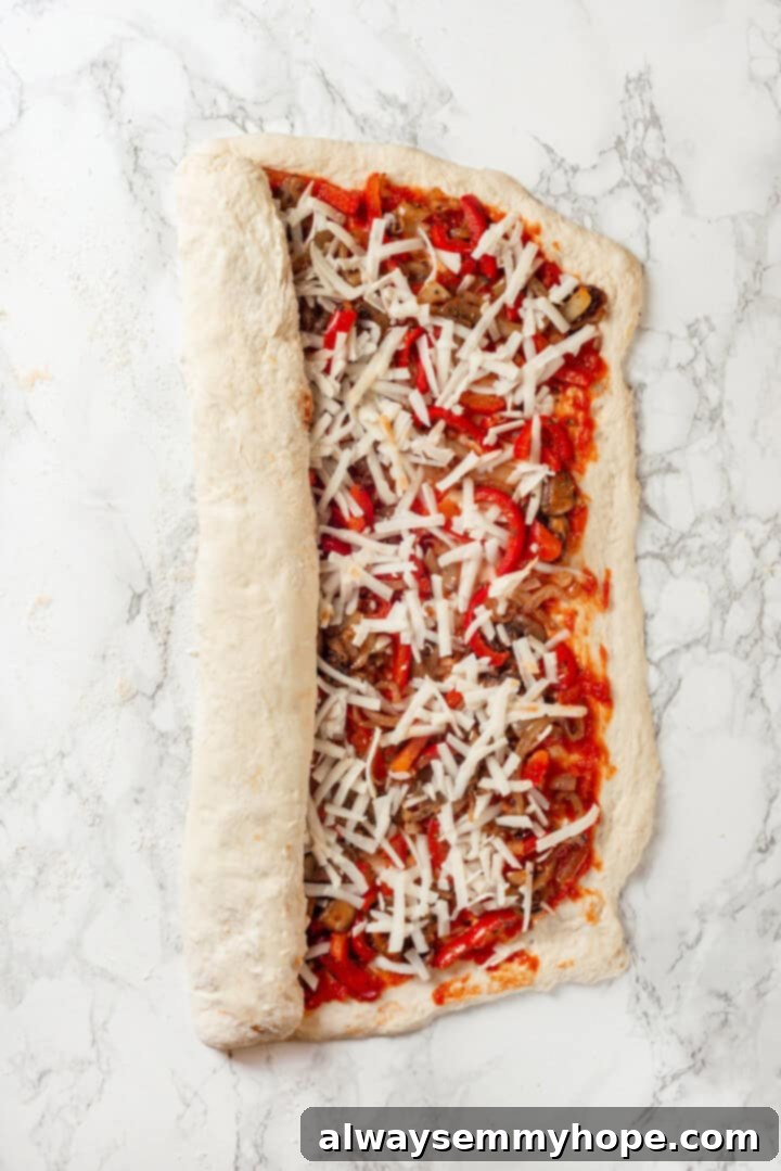 This vegan stromboli recipe is like a giant pizza roll, with marinara, plant-based cheese and veggies baked inside a golden brown crust. Yum! Overhead view of stromboli being rolled up