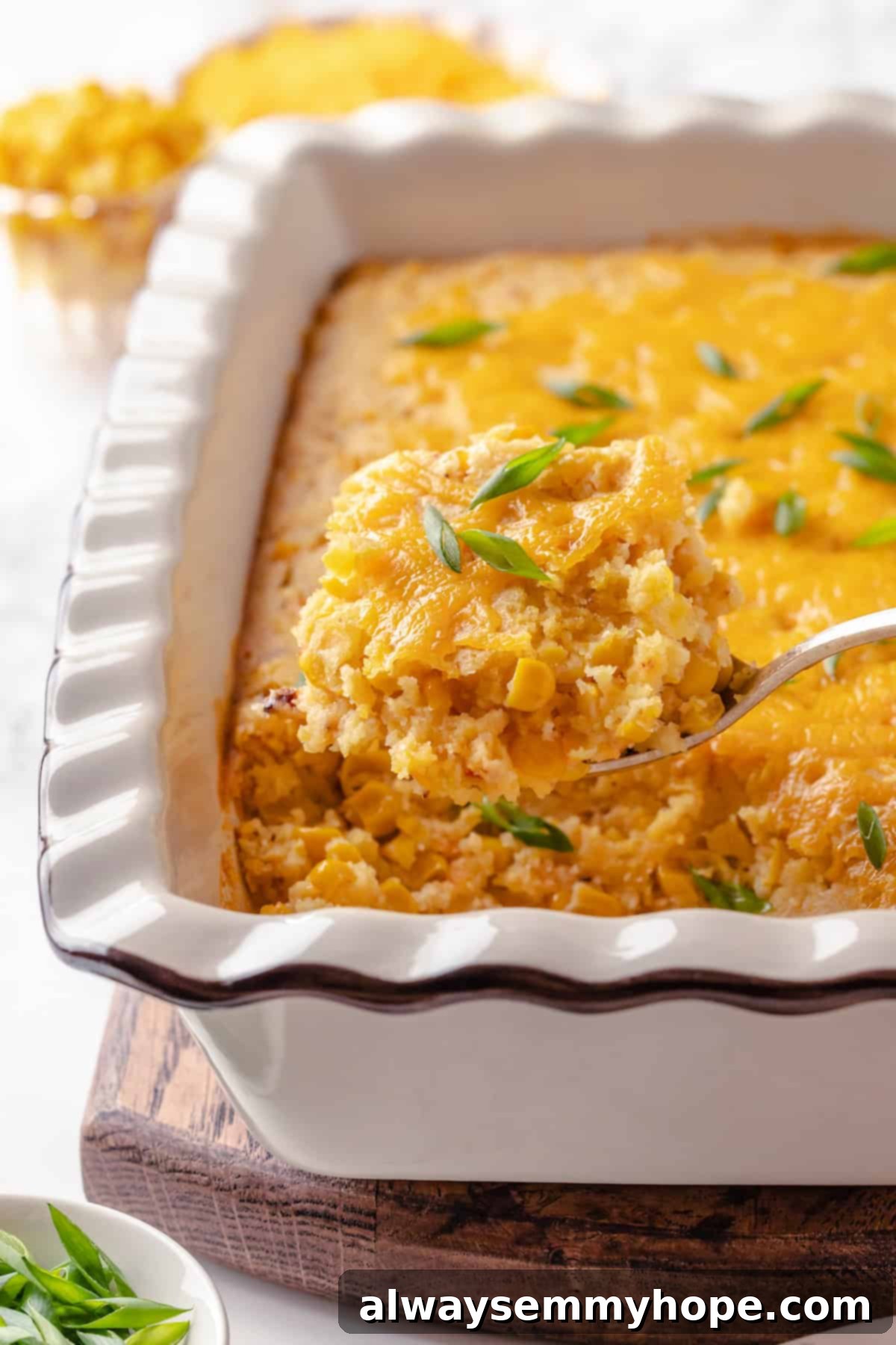 This easy vegan corn casserole is creamy, cheesy and sweet, with all the flavour you love of the holiday classic. Always a crowd-plaser! A serving spoon lifting a generous portion of creamy vegan corn casserole out of the baking dish, showcasing its texture and warm appeal.