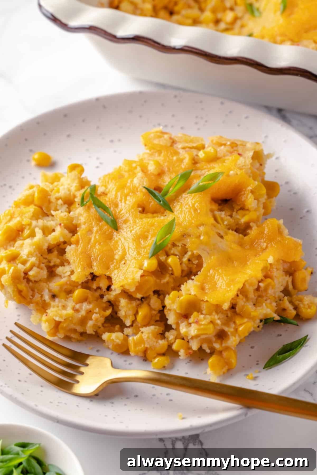 This easy vegan corn casserole is creamy, cheesy and sweet, with all the flavour you love of the holiday classic. Always a crowd-pleaser! A delectable serving of creamy vegan corn casserole on a white plate with a fork, showing its soft interior and golden-brown top.