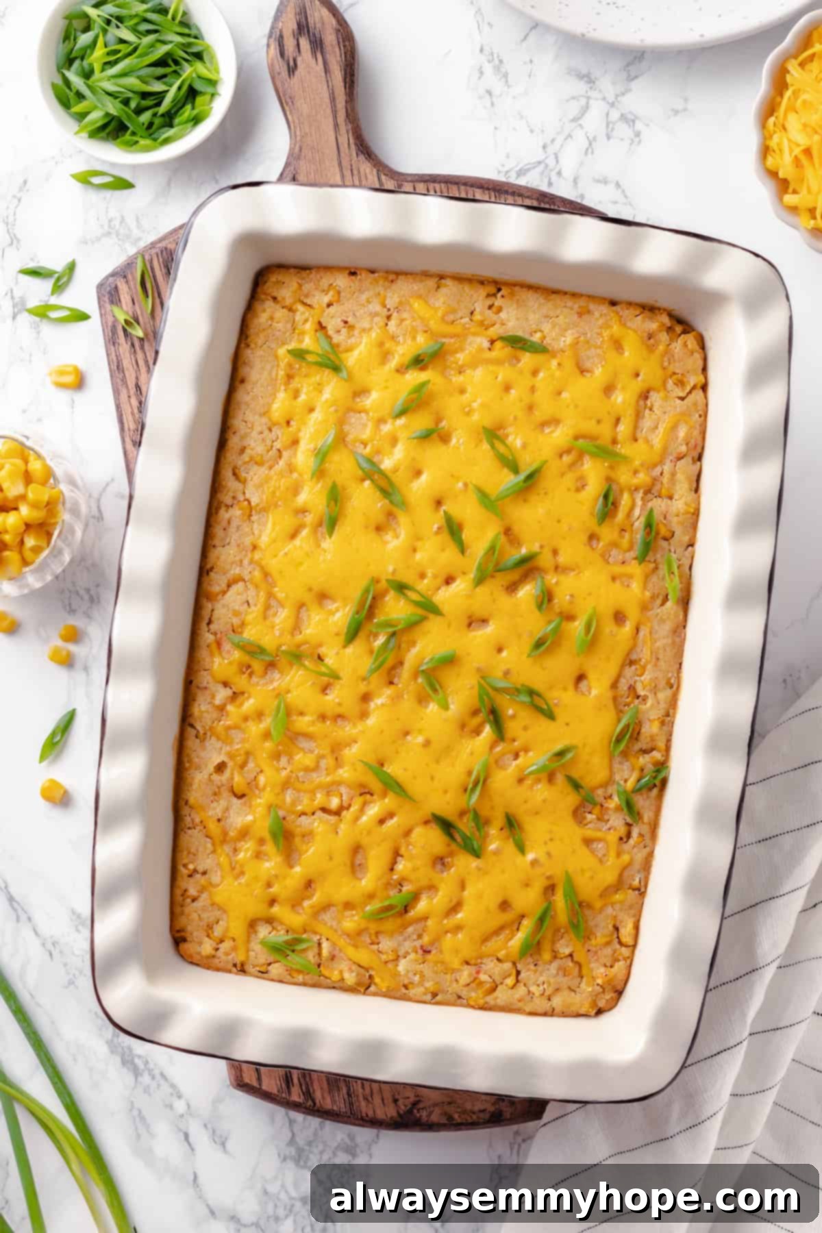 This easy vegan corn casserole is creamy, cheesy and sweet, with all the flavour you love of the holiday classic. Always a crowd-pleaser! Top-down view of a golden-brown vegan corn casserole topped with bubbling melted vegan cheese in a ceramic baking dish, fresh from the oven.
