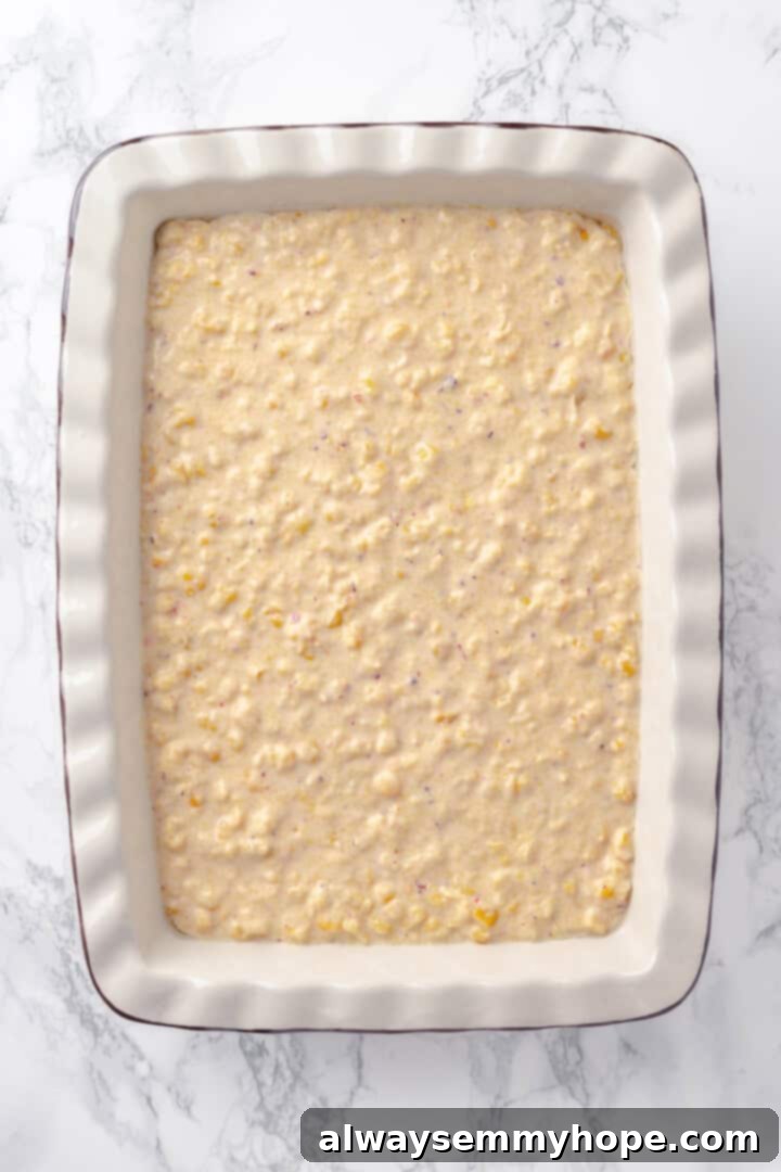 This easy vegan corn casserole is creamy, cheesy and sweet, with all the flavour you love of the holiday classic. Always a crowd-pleaser! Overhead view of the vegan corn casserole mixture spread evenly into a greased baking dish, ready to be placed in the oven.