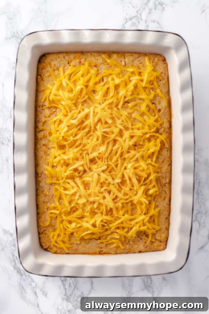 This easy vegan corn casserole is creamy, cheesy and sweet, with all the flavour you love of the holiday classic. Always a crowd-pleaser! Overhead view of shredded vegan cheddar cheese generously sprinkled over the top of the partially baked vegan corn casserole, ready for final melting.