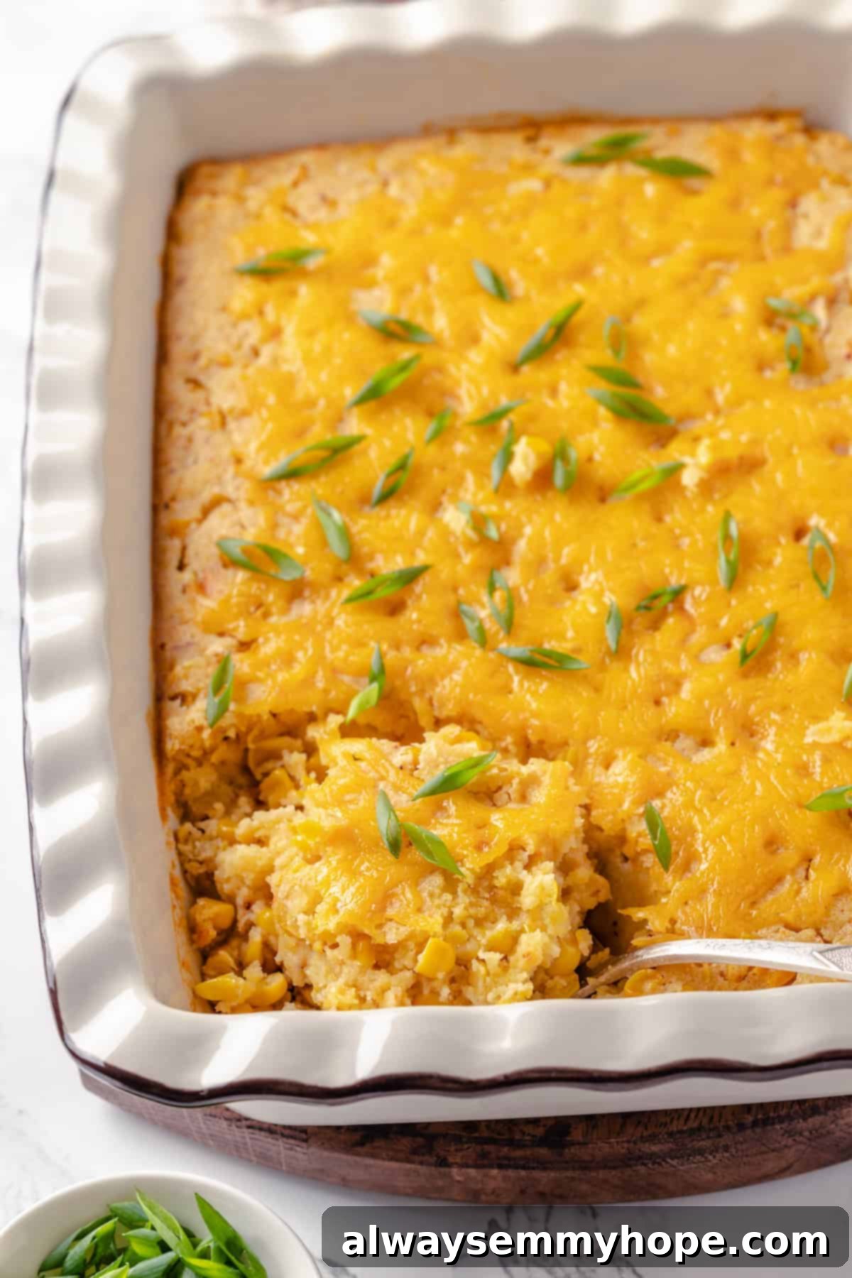 This easy vegan corn casserole is creamy, cheesy and sweet, with all the flavour you love of the holiday classic. Always a crowd-pleaser! A serving spoon digging into the creamy and golden vegan corn casserole in a baking dish, highlighting its rich texture and melted cheese.