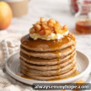 Stack of apple pie pancakes on plate with yogurt, syrup, and apples on top