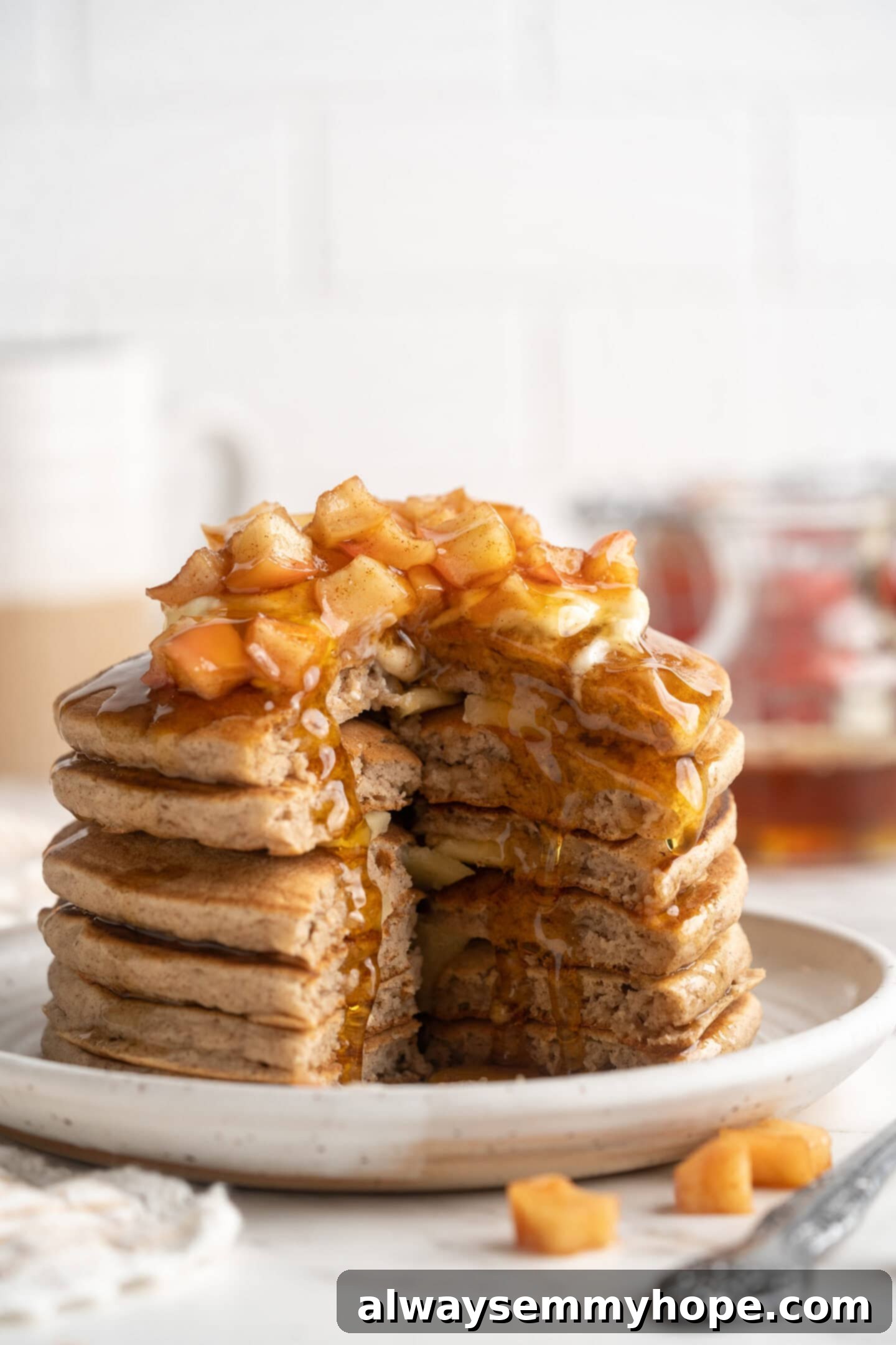A beautifully composed stack of vegan apple pie pancakes, topped with more fresh apple slices and a light dusting of cinnamon, presented on a plate. The soft, inviting texture of the pancakes is evident, making them look utterly delicious and ready to be enjoyed.