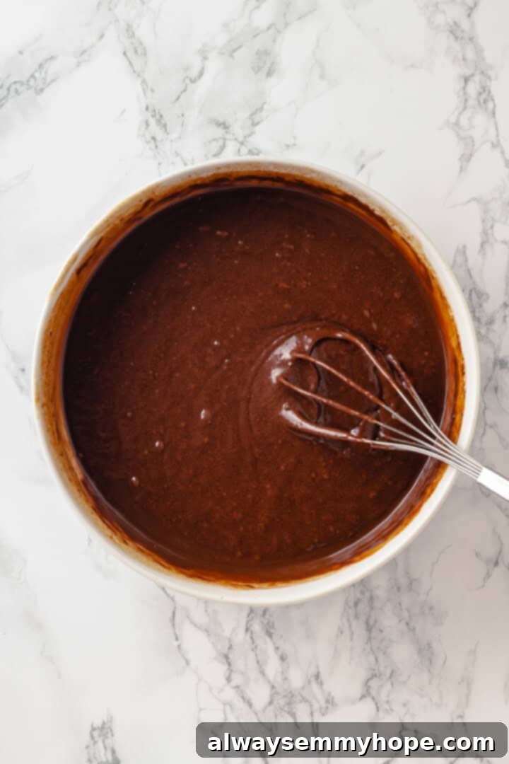 These moist chocolate Halloween cupcakes are topped with cute frosting monsters in a variety of colours. They taste as good as they look! Vegan chocolate cupcake batter in a bowl with a whisk, showcasing the smooth, well-combined mixture of wet and dry ingredients before the final additions.
