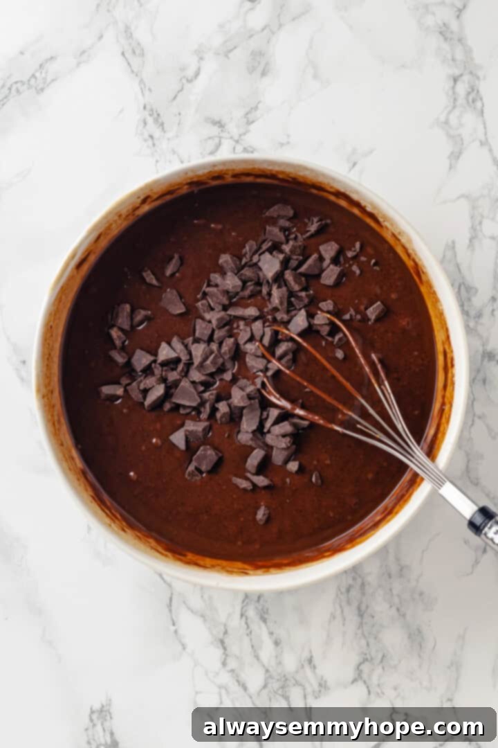 These moist chocolate Halloween cupcakes are topped with cute frosting monsters in a variety of colours. They taste as good as they look! Chopped vegan dark chocolate being added to a bowl of smooth chocolate cupcake batter, ready to be gently folded in for extra richness and texture.