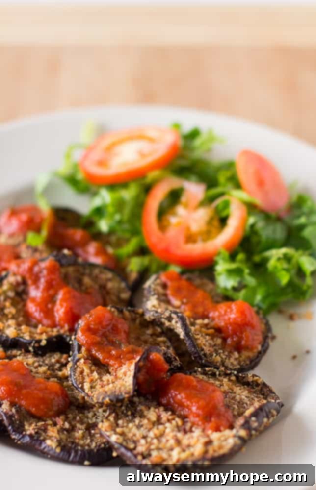 Almond-crusted baked eggplant slices served with a fresh green salad on a white plate, highlighting a healthy and vibrant meal.