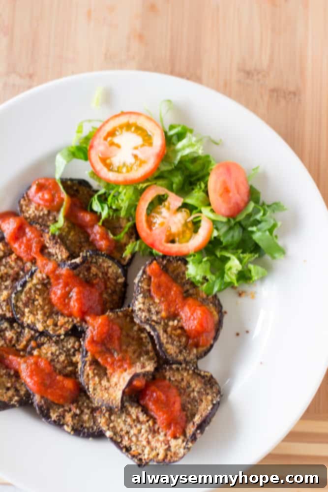 Overhead shot of freshly baked almond-crusted eggplant slices, golden and crispy, on a white plate, ready to be served.