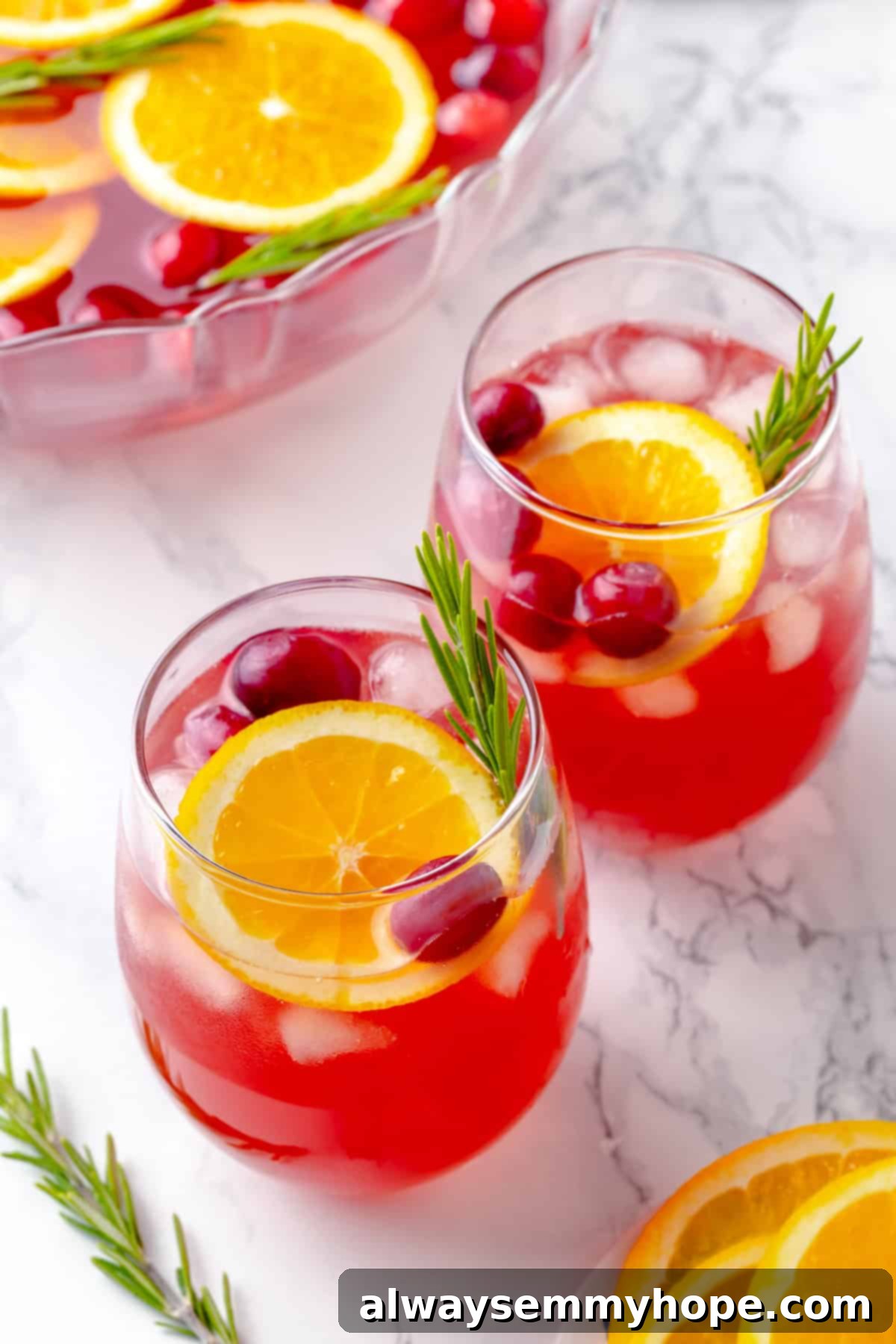 Two glasses of sparkling Christmas punch garnished with fresh cranberries, orange slices, and a sprig of rosemary.