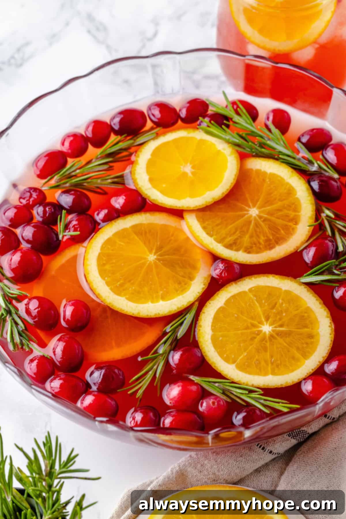 A beautiful bowl of Christmas punch garnished generously with fresh cranberries, bright orange slices, and fragrant rosemary sprigs.