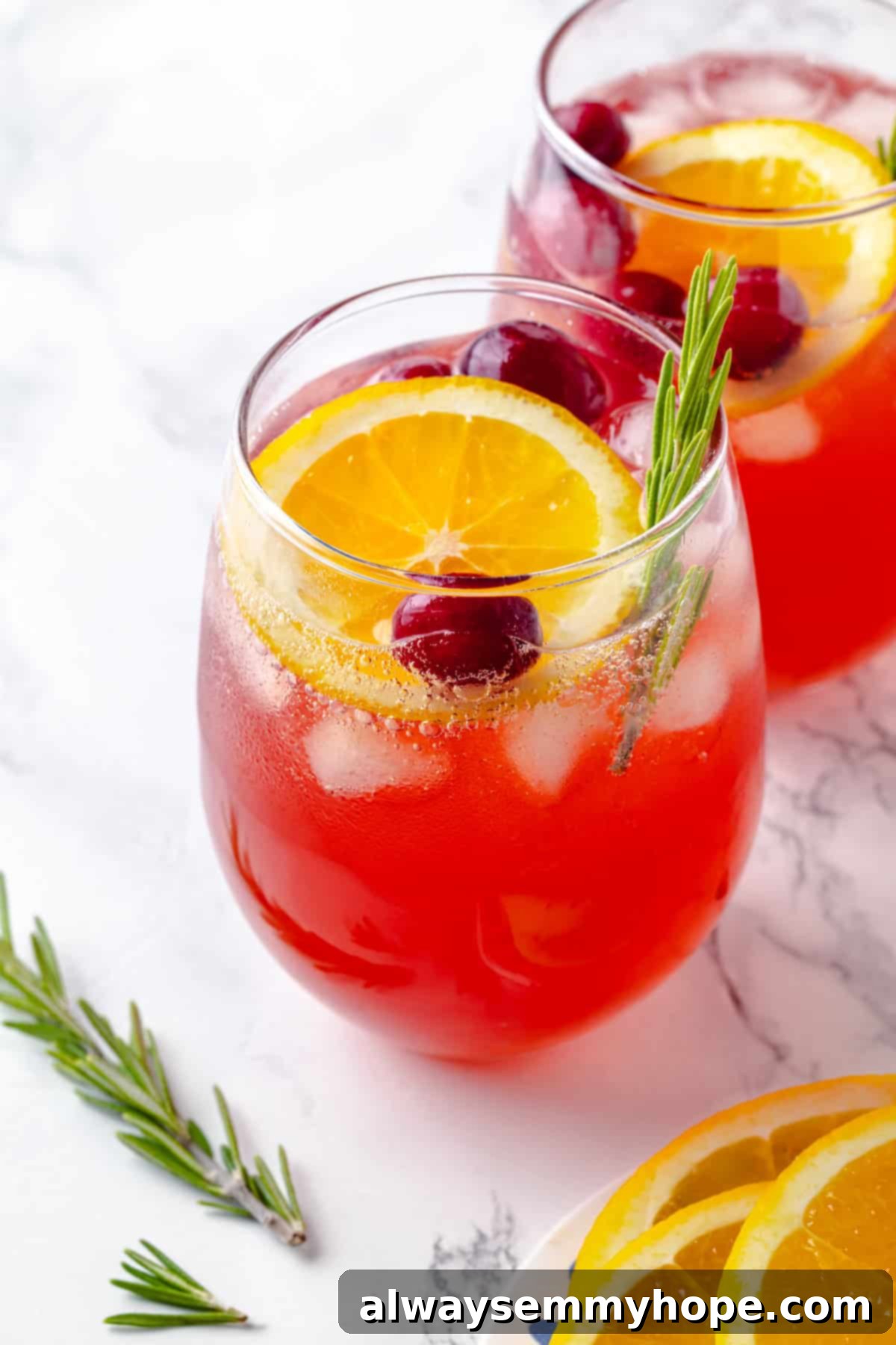 Two glasses of sparkling Christmas punch, beautifully garnished with orange slices, fresh rosemary, and cranberries, evoking a festive holiday mood.