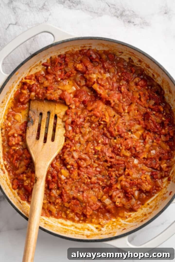 Overhead view of tomato sauce simmering in skillet with slotted spoon